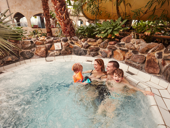 Een gezin met twee jonge kinderen ontspant samen in een warm bubbelbad in het tropische zwemparadijs Aqua Mundo van Center Parcs De Huttenheugte.