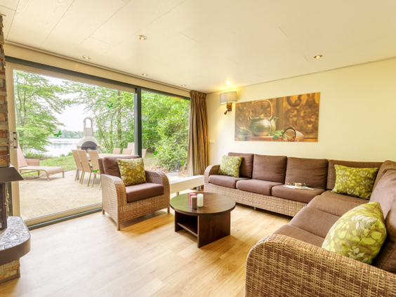 De sfeervolle woonkamer van een waterfront cottage bij Center Parcs De Huttenheugte, met een grote schuifpui die direct toegang geeft tot het terras aan het meer.