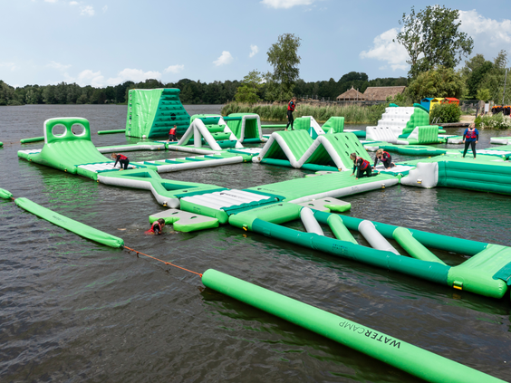 Het grote, opblaasbare Aquapark met hindernissen en glijbanen ligt op het meer van Center Parcs De Huttenheugte op een zonnige dag.