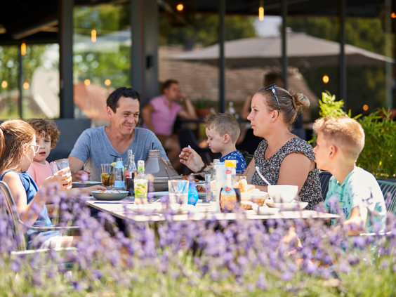 Een gezin met drie kinderen geniet van een maaltijd op het zonnige terras van restaurant Buitenhof op Recreatiepark De Leistert, omringd door lavendel.