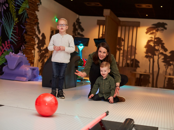 Een moeder en haar twee zonen spelen een spel met een rode bal op een interactieve speelvloer bij de bowlingbaan op Recreatiepark De Leistert.
