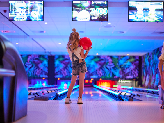 Een meisje staat klaar om een rode bowlingbal te gooien op een van de kleurrijk verlichte bowlingbanen op Recreatiepark De Leistert.