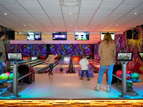 Families met kinderen zijn aan het bowlen op de moderne, met discoverlichting verlichte bowlingbanen van Recreatiepark De Leistert.