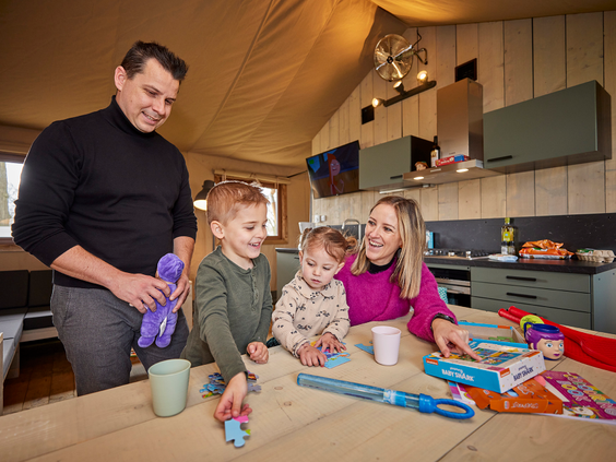 Familie speelt samen aan de eettafel in een safaritent in een ruime en luxe ingerichte safaritent op De Leistert.