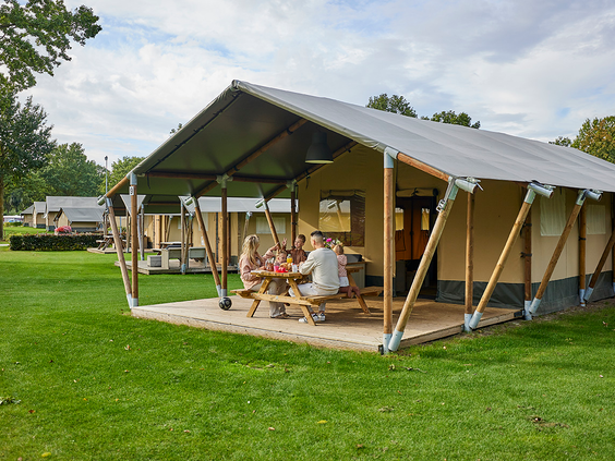 Een luxe safaritent met een houten veranda en een picknicktafel op een ruim grasveld op Recreatiepark De Leistert.