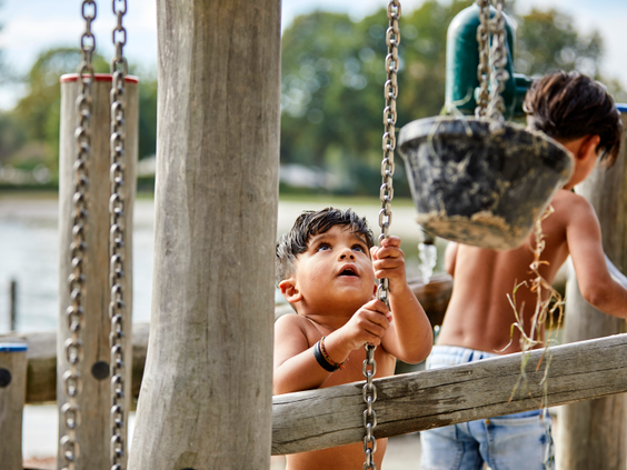 Twee jonge kinderen spelen met water en zand bij een houten speeltoestel met emmertjes en kettingen in de waterspeeltuin aan het strand van De Leistert.