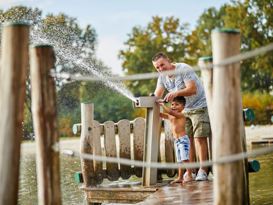 Een vader en zoon spelen samen met een groot waterkanon op een houten vlonder bij de recreatieplas van De Leistert.