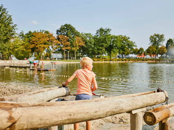 Een kind speelt met houten watergoten aan de rand van de recreatieplas op het dagstrand van Recreatiepark De Leistert.