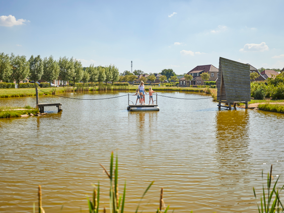 Drie kinderen staan op een houten trekvlot en trekken zichzelf naar de overkant van de roei- en speelvijver op Recreatiepark De Leistert.