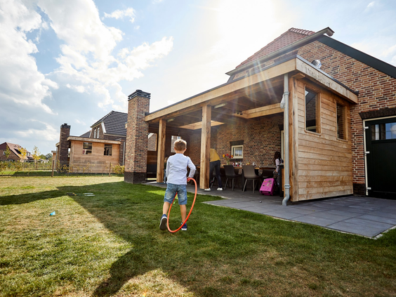 Een jongen speelt met een hoepel op het grote grasveld achter een luxe, houten vakantieboerderij op Recreatiepark De Leistert.