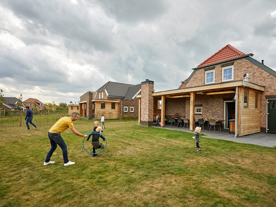 Een familie speelt met een hoepel op het grote grasveld achter hun luxe vakantieboerderij op Recreatiepark De Leistert.