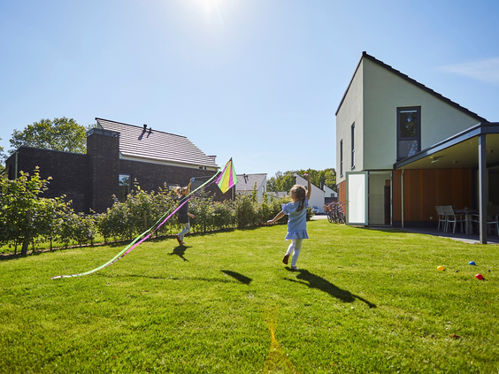 Een kind rent met een vlieger door de grote, zonnige tuin van een modern vakantiehuis op Recreatiepark De Leistert.