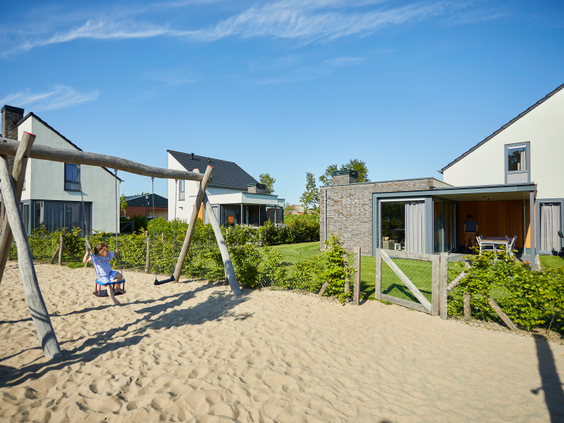 Een kind schommelt in de zandspeeltuin die direct gelegen is bij de moderne vakantiehuizen op Recreatiepark De Leistert.