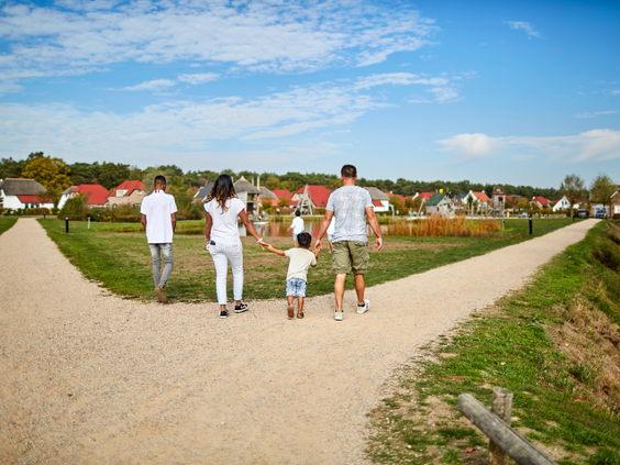 Een gezin met twee kinderen wandelt hand in hand over een onverhard pad op het uitgestrekte terrein van Recreatiepark De Leistert.
