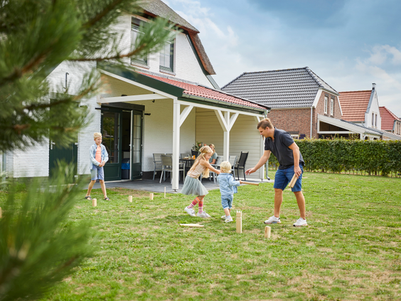 Een familie speelt het populaire werpspel Kubb op het grasveld in de tuin van hun vakantiehuis op Recreatiepark De Leistert.
