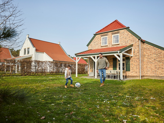 Een vader en zoon spelen voetbal op het grote grasveld in de tuin van hun vakantiehuis op Recreatiepark De Leistert.