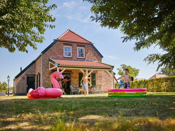 Kinderen spelen in een opblaasbaar zwembadje in de tuin van een vakantieboerderij, met een grote roze flamingo ernaast.