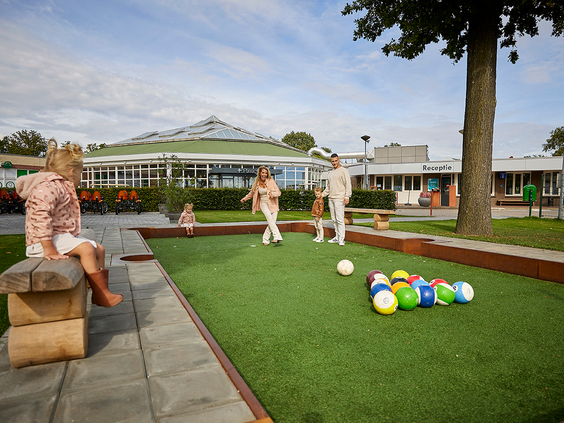 Een familie speelt een potje voetbalbiljart op de speciale baan op het buitenterrein van Recreatiepark De Leistert, bij het overdekte terras.