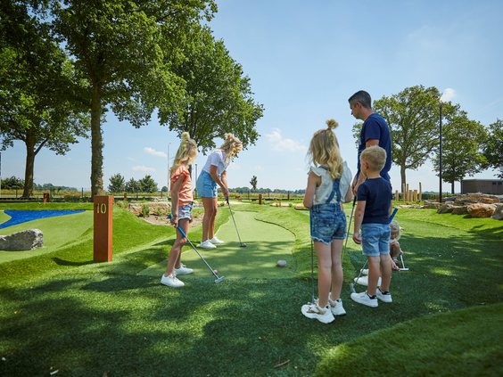 Een gezin met drie kinderen speelt midgetgolf op de avontuurlijke en groen aangelegde golfbaan van Recreatiepark De Leistert.