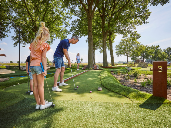 Een vader slaat de golfbal terwijl zijn kinderen toekijken tijdens een potje midgetgolf op de avontuurlijke golfbaan van De Leistert.