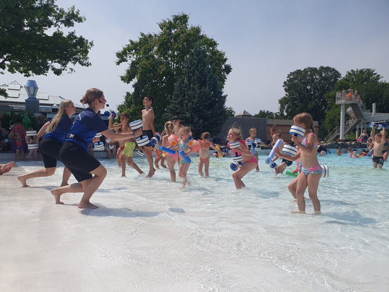 Een groep kinderen doet samen met het animatieteam yoga-oefeningen en rekoefeningen tijdens een aquagym-les in het buitenzwembad van De Leistert.