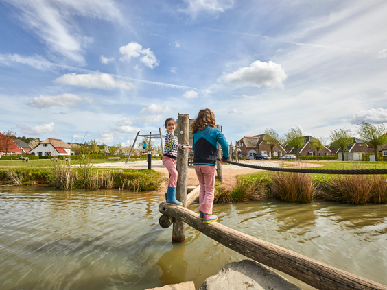 Twee meisjes balanceren op een houten boomstam over de speelvijver op Recreatiepark De Leistert.