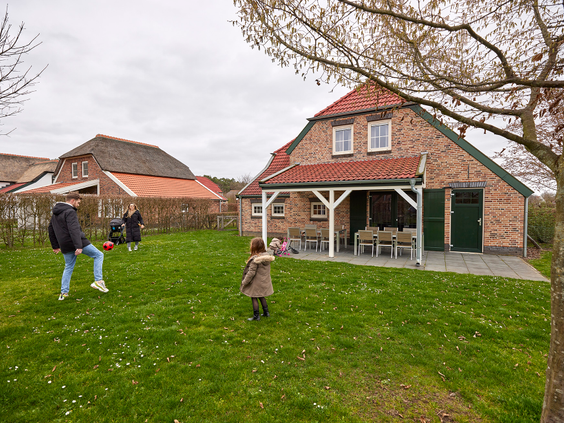 Een familie speelt samen op het grote grasveld voor hun vakantieboerderij op Recreatiepark De Leistert.