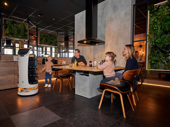 Een gezin met twee jonge kinderen wordt bediend door een rijdende serveerrobot in een modern restaurant op Recreatiepark De Leistert.