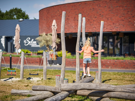 Een meisje balanceert op een houten evenwichtsbalk in de avontuurlijke buitenspeeltuin bij restaurant Buitenhof De Leistert.