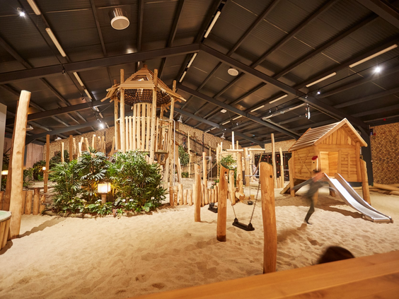 Overzicht van het grote indoor speelparadijs La Selva op Recreatiepark De Leistert, met houten klimtoestellen en een zandvloer.