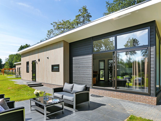 Zonnig en ruim terras van een moderne lodge op Vakantiepark De Lochemse Berg, met een comfortabele loungeset en uitzicht op de tuin.