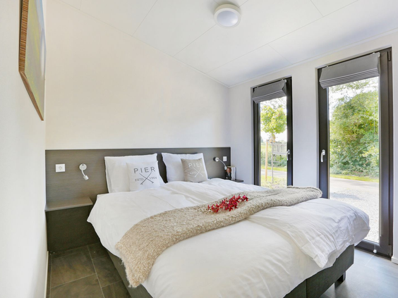 Comfortabele tweepersoons slaapkamer in een lodge op Vakantiepark De Lochemse Berg, met openslaande deuren naar de groene tuin