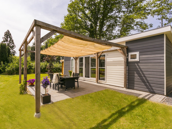 Een sfeervol, overdekt terras met een pergola en schaduwdoek bij een vakantielodge op De Lochemse Berg in de Achterhoek.