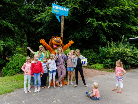 Een grote groep blije kinderen die op de foto gaan met de vrolijke mascotte Alex Avontuur op RCN de Roggeberg.