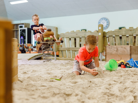 Kinderen die heerlijk spelen in de grote overdekte binnenzandbak op RCN de Roggeberg, ideaal voor als het weer even wat minder is.