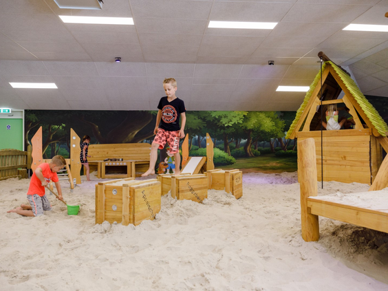 Kinderen die spelen in de ruime binnenspeeltuin met een grote zandbak en houten speeltoestellen op RCN de Roggeberg.