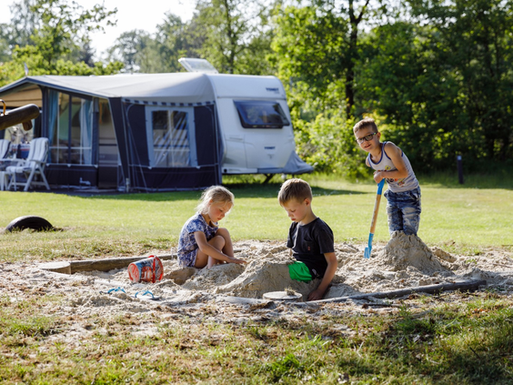 Drie kinderen die samen zandkastelen bouwen in de zandbak op de camping, een leuke speelplek voor nieuwe vakantievriendjes.