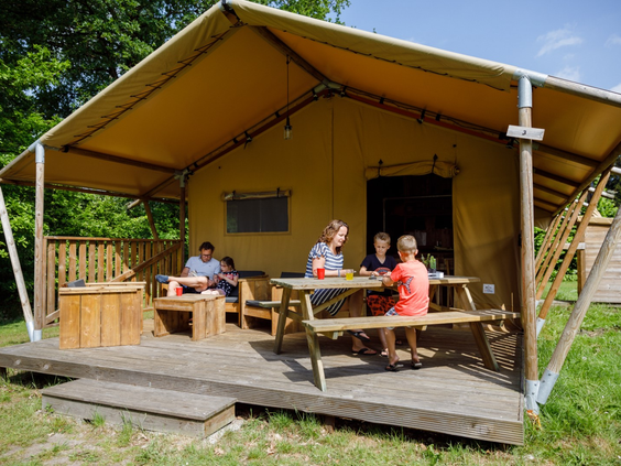 Een gezin geniet op de ruime houten veranda van een luxe safaritent op RCN de Roggeberg, de ideale glamping-ervaring.