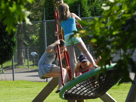 Drie kinderen hebben plezier op een grote nestschommel in de buitenspeeltuin van Recreatiepark De Scherpenhof in Gelderland.