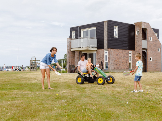 Een gezin vermaakt zich op het grasveld bij hun vakantiehuis op RCN de Schotsman in Zeeland, met een skelter en een potje badminton.