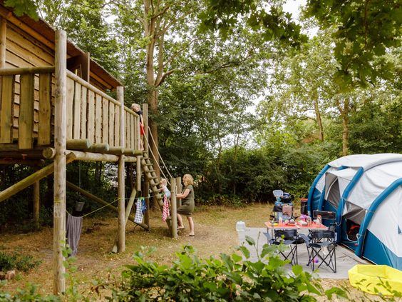Unieke kampeerplaats op RCN de Schotsman met een eigen houten speeltoestel in de vorm van een boomhut, direct naast de tent.