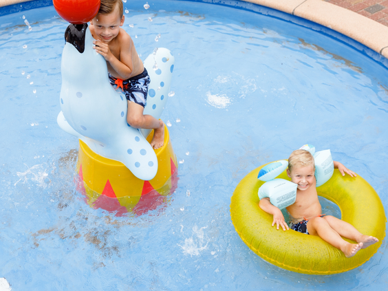 Twee jonge kinderen spelen in het verwarmde peuterbad van RCN de Schotsman, met een speelse zeehond en een zwemband.