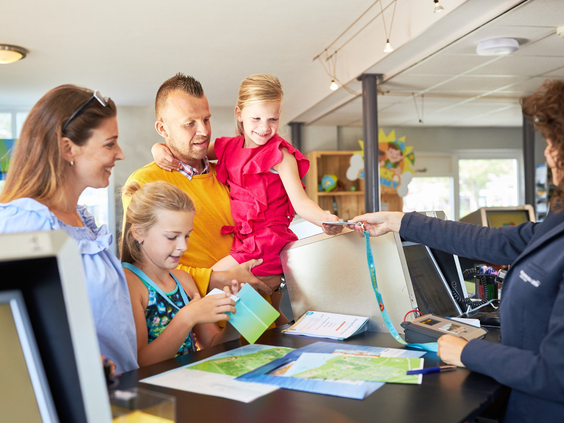 Een gezin met twee dochters checkt in bij de receptie van RCN de Schotsman en ontvangt informatie voor hun vakantie.
