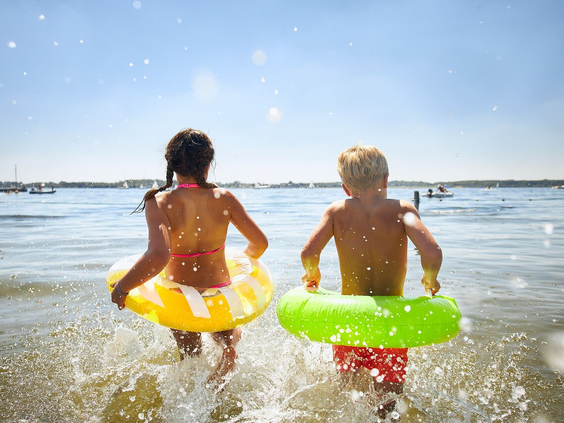 Twee kinderen met zwembanden rennen het ondiepe water van het Veerse Meer in voor een dag vol waterpret bij RCN de Schotsman.