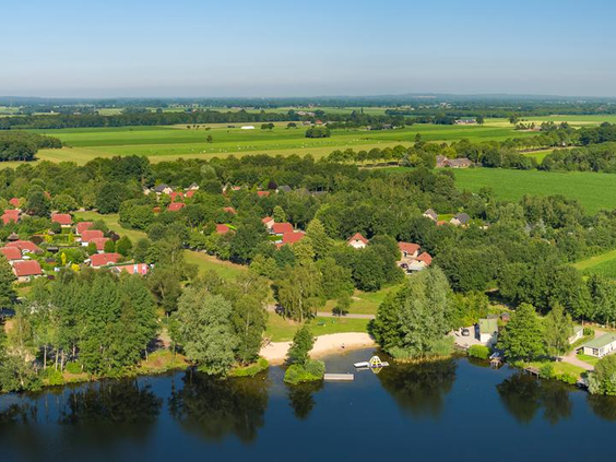 Luchtfoto van vakantiepark De Tolplas, met de grote recreatieplas in het midden, omringd door vakantiehuisjes en de groene natuur van Twente.