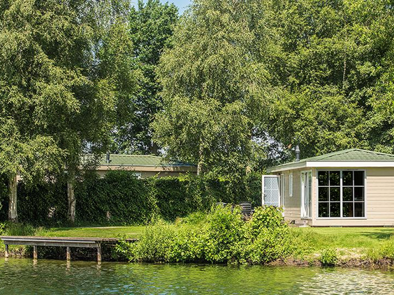 Een wit vakantiehuis op De Tolplas, idyllisch gelegen aan de waterkant met een eigen vlonder en omgeven door hoge bomen.