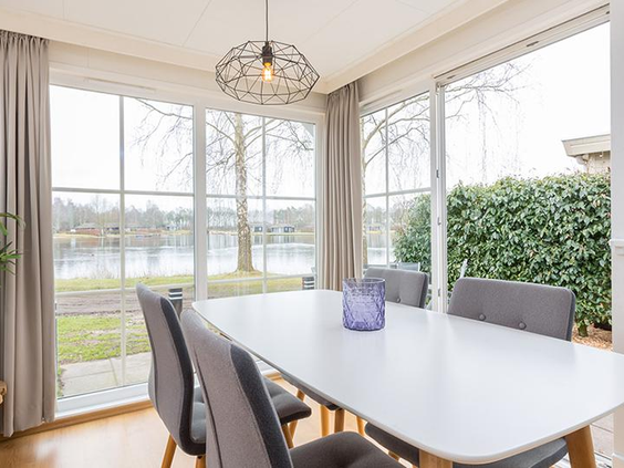 Moderne eethoek in een vakantiehuis op De Tolplas met een grote eettafel en stoelen, en via de grote ramen prachtig uitzicht over de recreatieplas.
