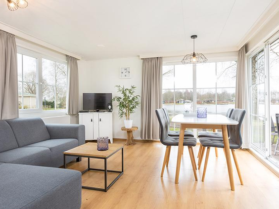 Lichte en moderne woonkamer van een vakantiehuis op De Tolplas, met een comfortabele zithoek, eethoek en grote ramen met uitzicht naar buiten.