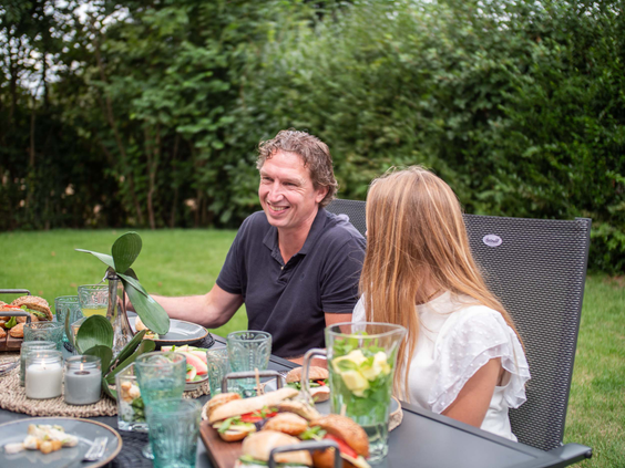 Een vader en dochter zitten lachend aan een gedekte tuintafel en genieten van een maaltijd in de buitenlucht op De Wielerbaan.
