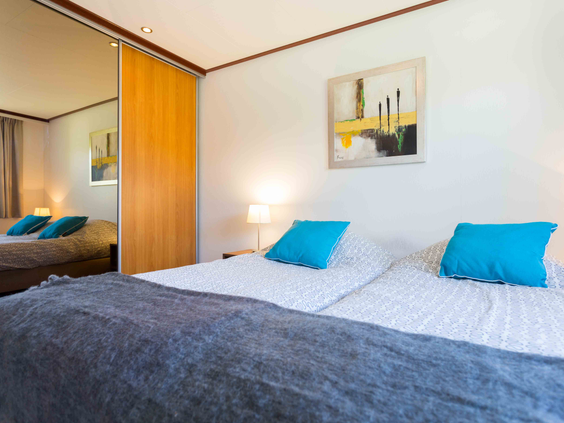 Nette slaapkamer met een comfortabel opgemaakt tweepersoonsbed en vrolijke blauwe kussens in een chalet op De Wielerbaan.